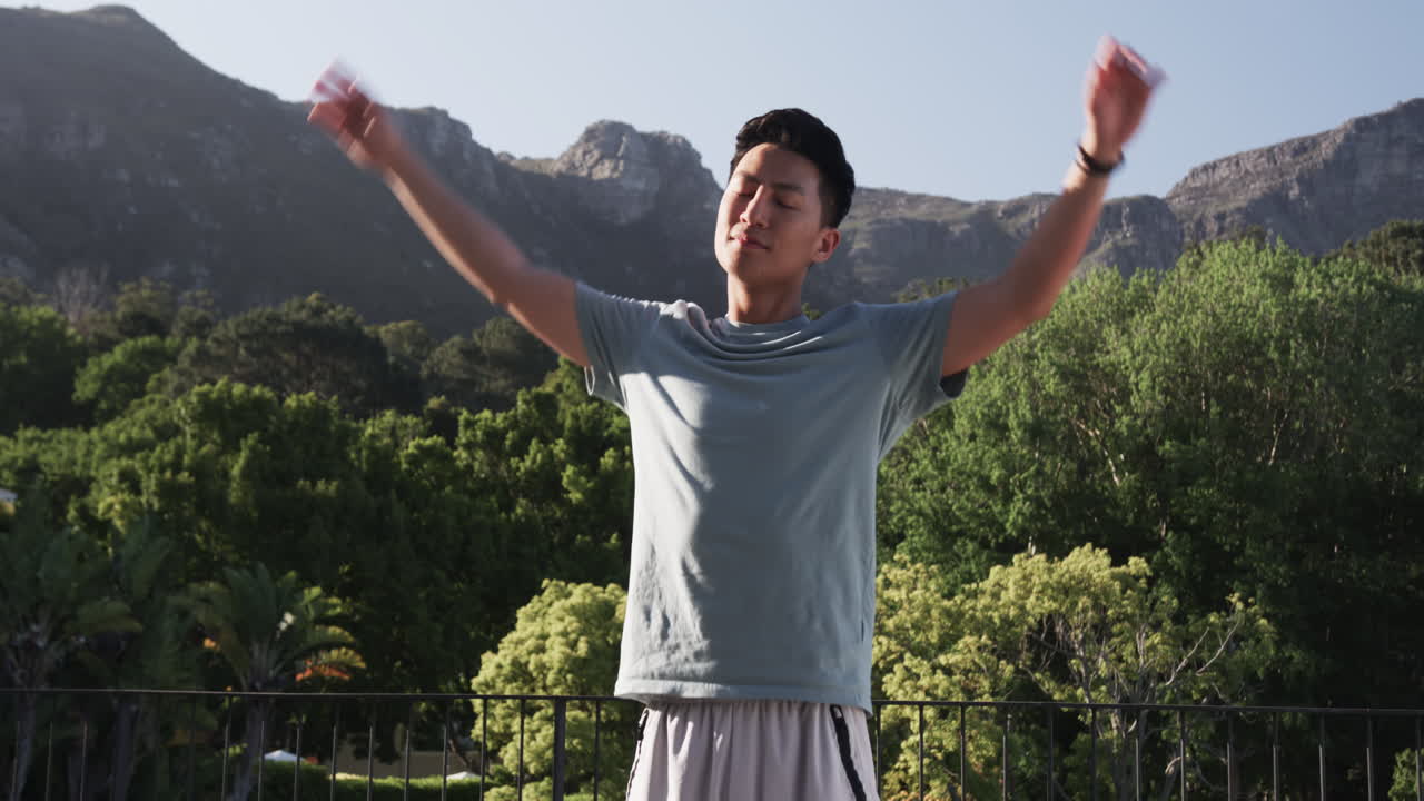 Asian man stretching outdoors with mountain view, enjoying morning exercise, on balcony, copy space