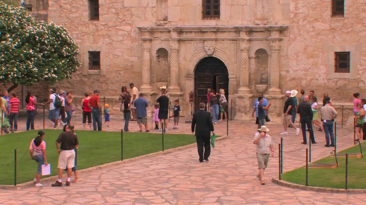 사람들은 텍사스 샌안토니오에 있는 돌 안뜰과 건물을 돌아다닙니다.