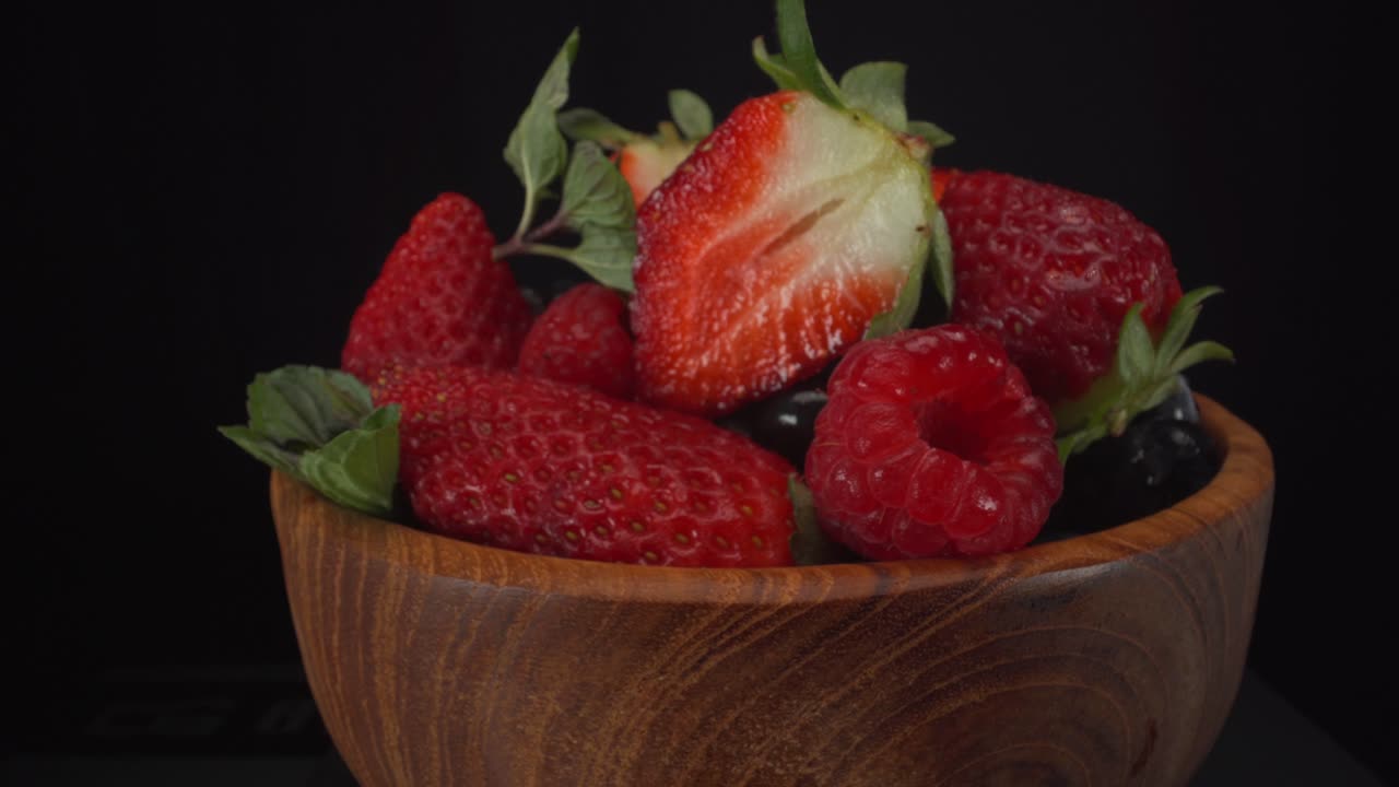 Incredibly juicy rotating forest fruits in a wooden bowl with black background, strawberries, blueberries, raspberries, healthy fruits, 4K shot