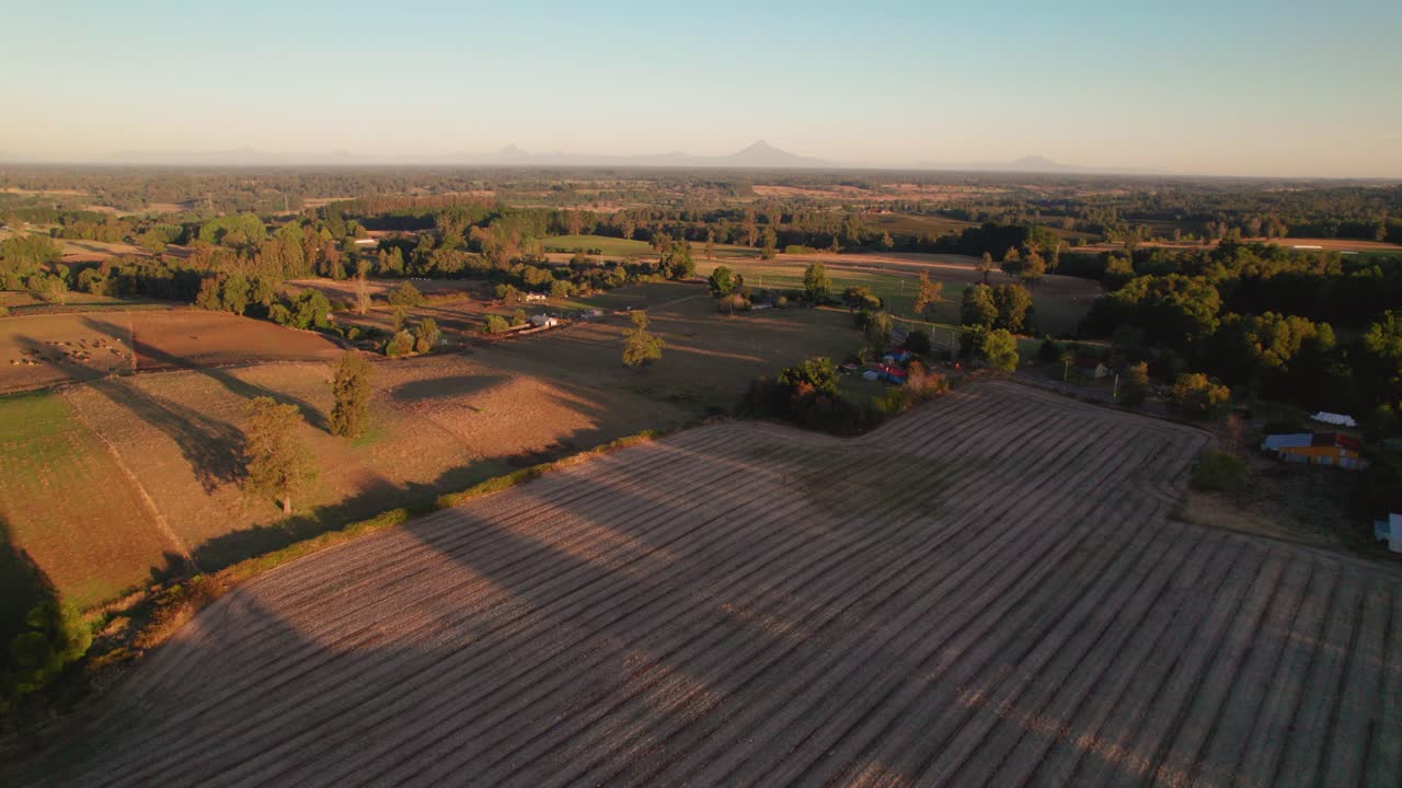 The fading light of the sun illuminates the winding dirt roads and rustic barns of a picturesque rural landscape, painting the sky with a beautiful array of colors
