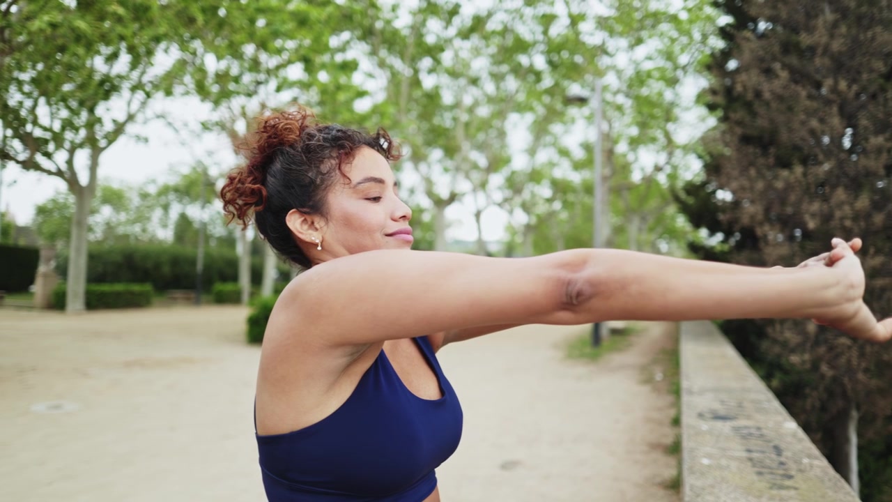 Mujer joven atándose el pelo y estirándose en un parque