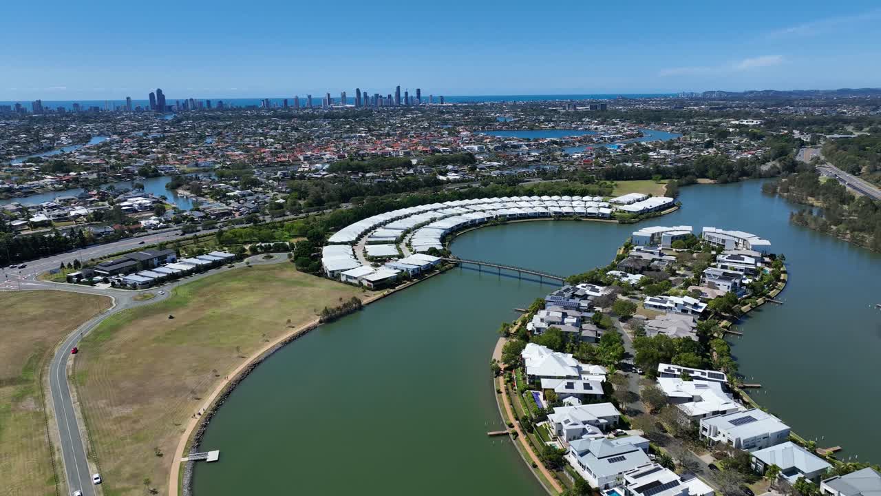 Drone footage capturing Emerald Lakes on the Gold Coast with Surfers Paradise skyline on the horizon—lush greenery, calm waters, and city skyscrapers shimmering in the distance.