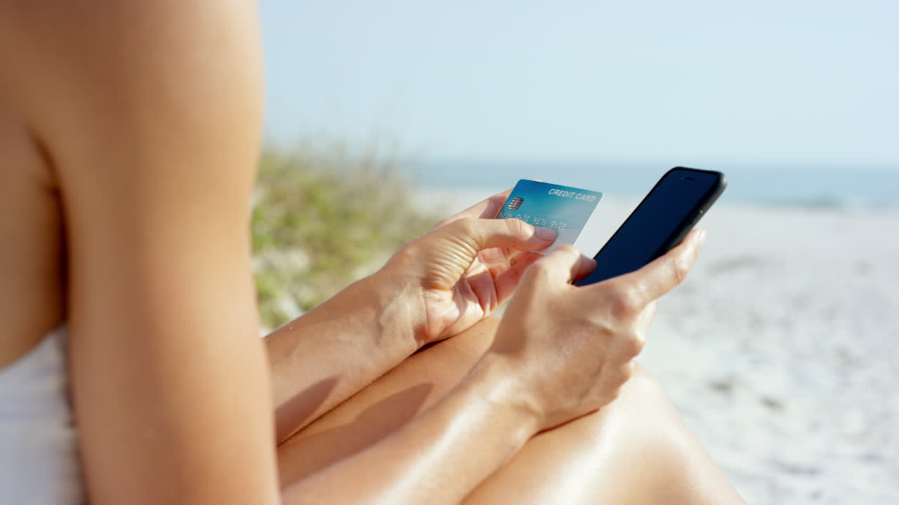 mujer de cerca usando tarjeta de crédito comprando en línea con teléfono móvil en la playa de vacaciones