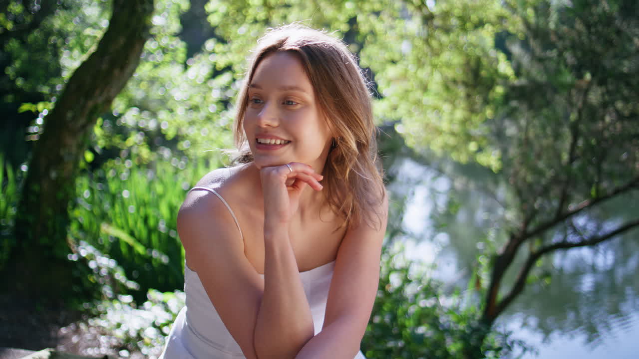 Sunshine woman video call talking by cellphone at greenery waterfront closeup
