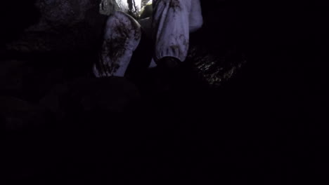 caver in white suit squeezes through tight restriction inside a cave