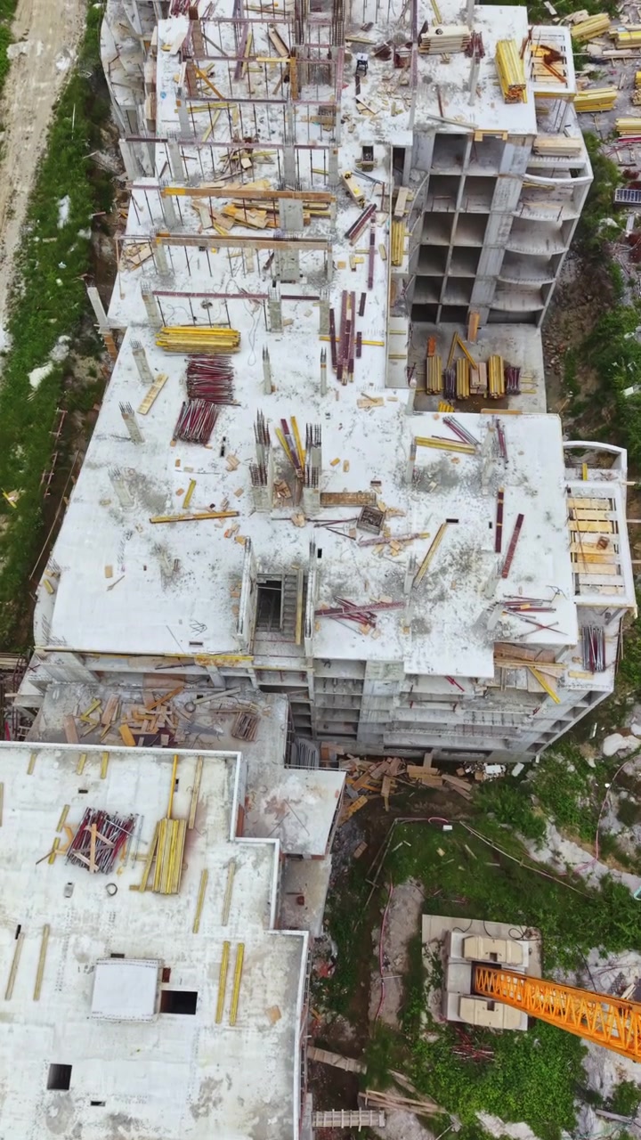 Trabajadores de la construcción ensamblan un edificio de varios pisos con grúas y materiales en un entorno urbano durante el día.