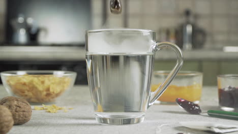 tea bag falls into a cup of hot water on a table prepared for breakfast