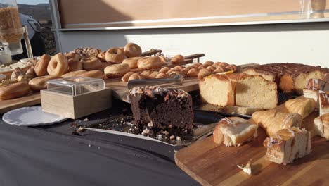 wooden boards and trays showcase an assortment of pastries, including sliced cakes, donuts, and croissants, arranged on a table with a black tablecloth