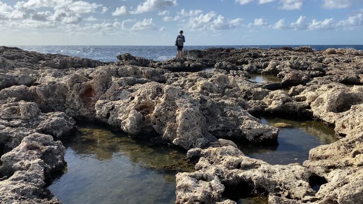Giovane viaggiatore che si gode le onde del mare che colpiscono la costa rocciosa di Malta