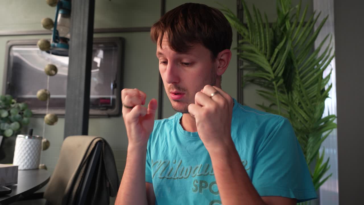 Frustrated man in casual clothes shows rising tension while seated at kitchen table, breathing and clenching attempting to self soothe through pain