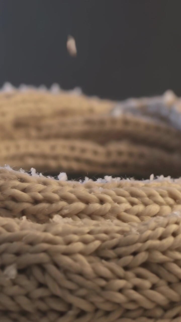 Video verticale: Particella bianca che cade e si posa su una maglia beige in una stanza poco illuminata, mostrando pillole.
