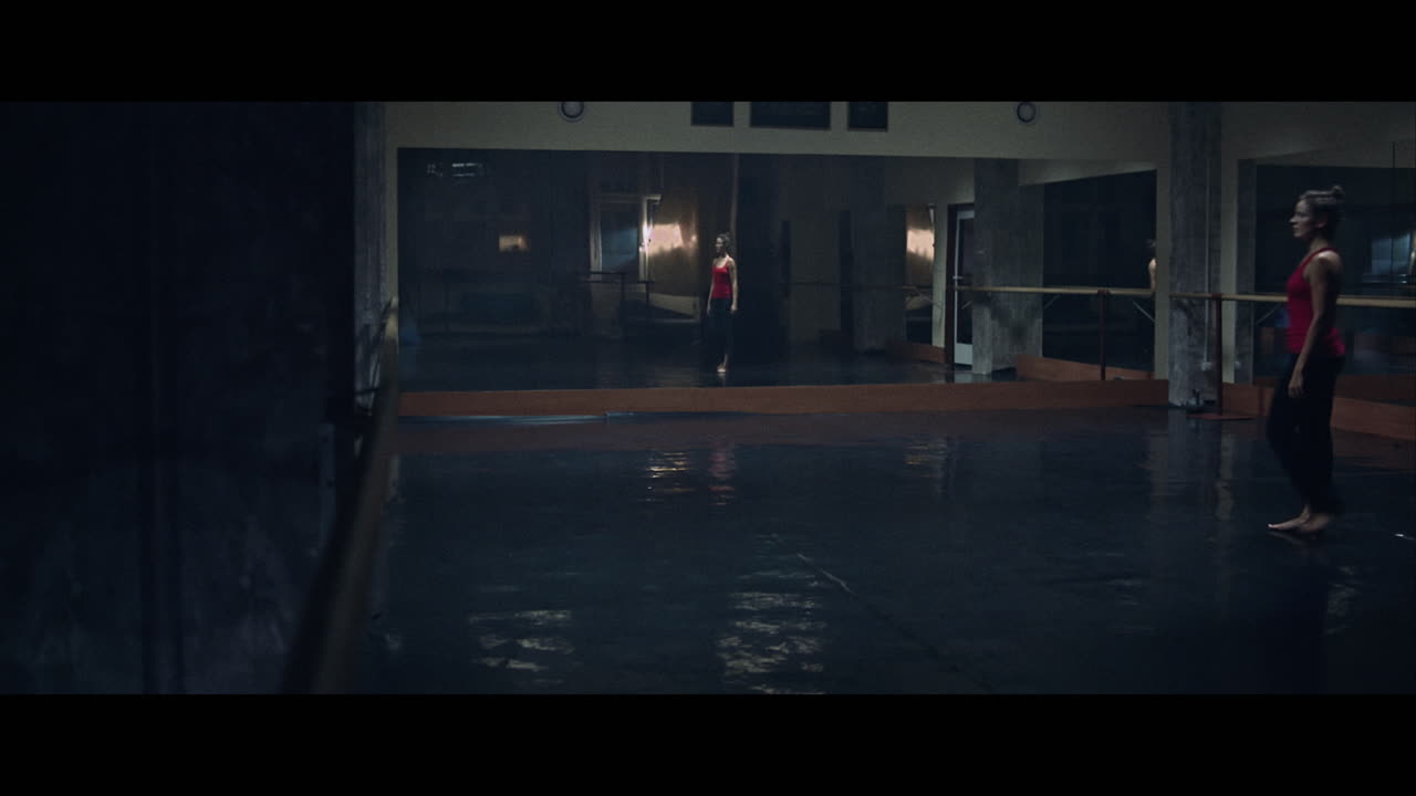 A young woman practices modern dancing and ballet in a moody room full of mirrors