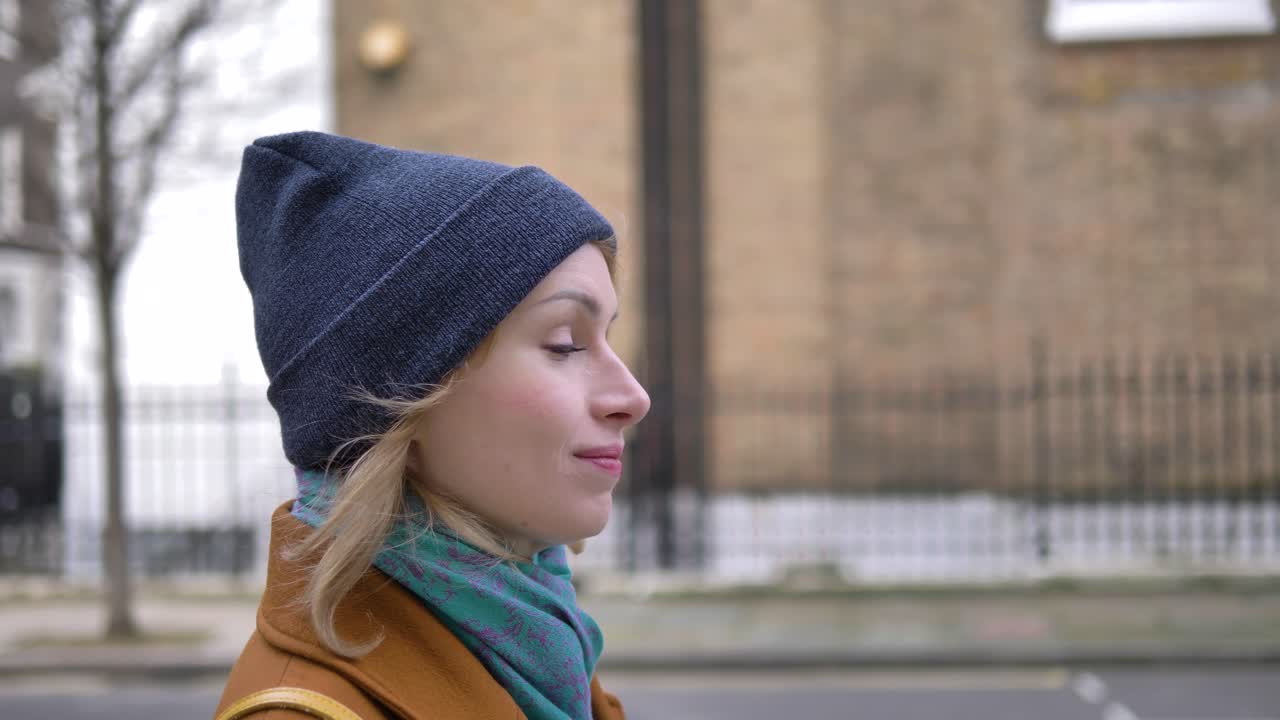 Side closeup view of a happy cheerful positive and relaxed young Caucasian woman enjoying the weather, walking down a London street and smiling while looking around