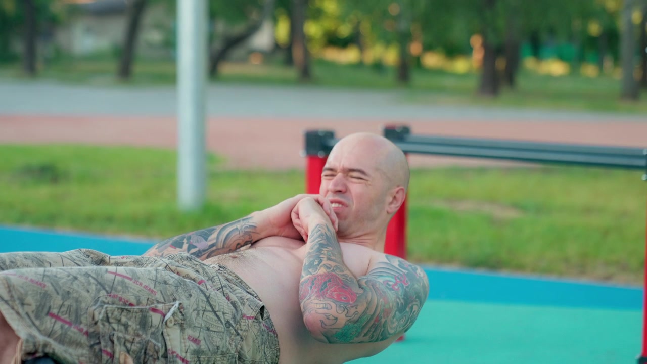 Glatzköpfiger, tätowierter Mann macht Sit-ups im Outdoor-Fitnessstudio