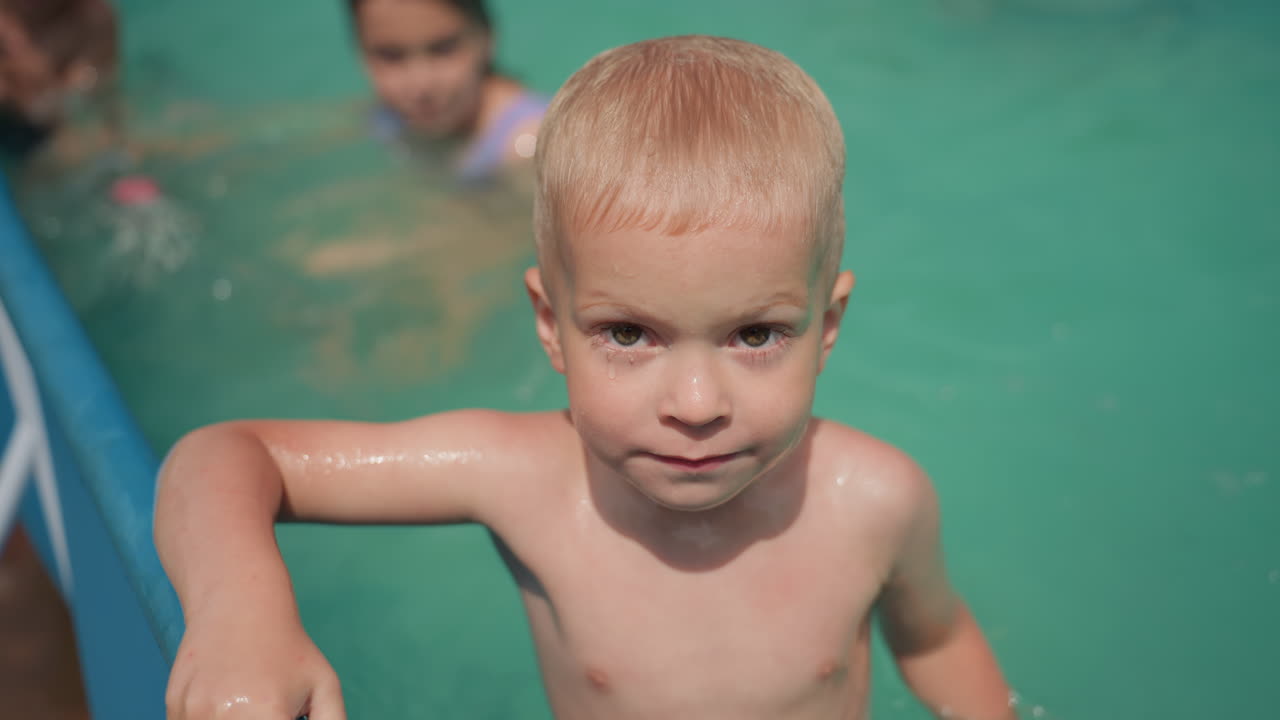 Child Observes Water, Focused Toddler Firmly Clutching Pool Boundary While Watching Water Closely, Child Attentively Observing Water While Holding Onto Pool Edge With Careful Grip And Concentration