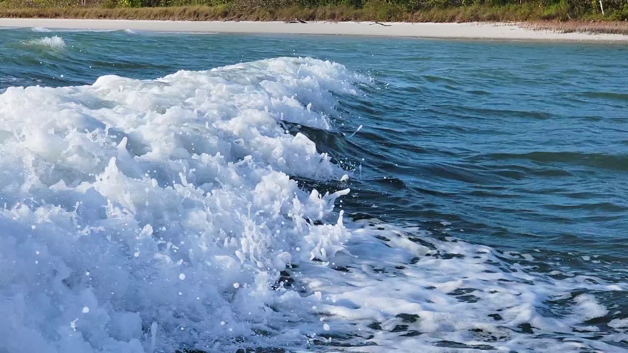 ondas de estela de barco cerca de lancha viajando junto a la playa en la corriente del océano con burbujas y chapoteando a lo largo de la costa de florida