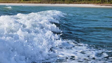 boat wake waves close up from motorboat traveling next to beach in the ocean current with bubbles and splashing along florida seashore