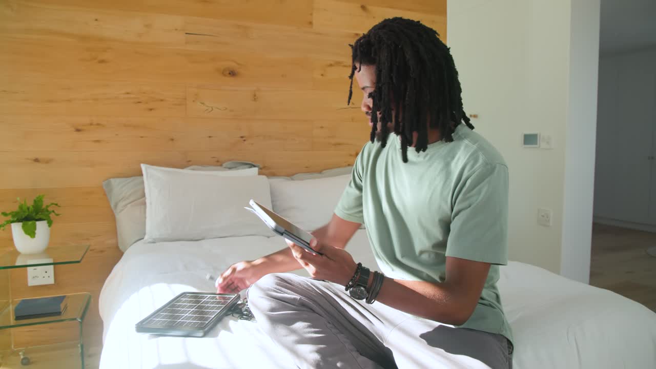 African American adult male reaching for tablet on bed, examining and swiping screens for reading