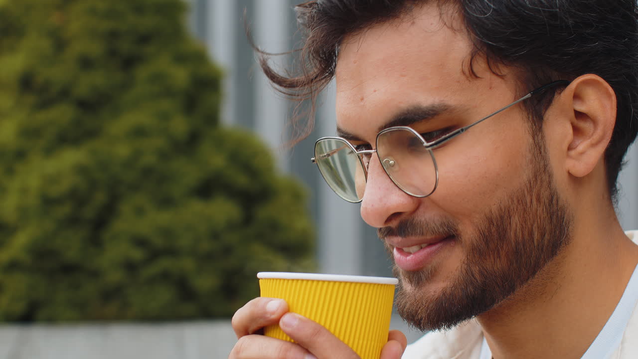 행복한 인도인 남자가 아침 커피를 즐기고 뜨거운 음료를 마시며 도시 거리에서 휴식을 취하고 휴식을 취합니다.