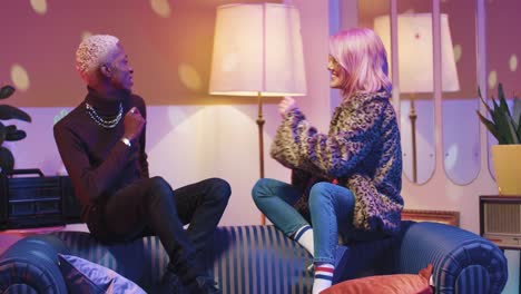 african american man and caucasian woman in sunglasses sitting on a sofa and dancing energetically in a retro party at home