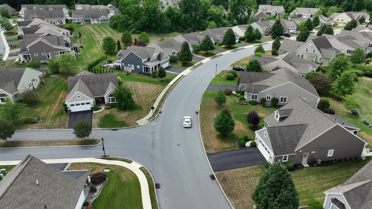 Aerial tracking shot of white car driving through modern and noble residential Area in summer