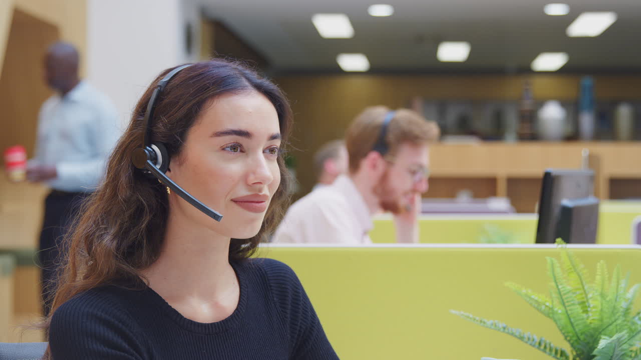 Portrait Of Businesswoman Wearing Headset Talking To Caller In Customer Services Centre