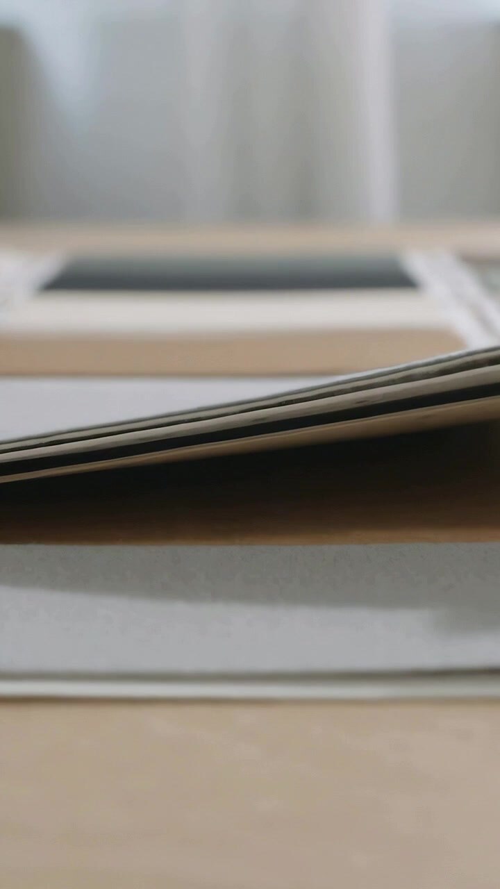 Vertical video: Window draft nudging paper stack and pads curling on wood desk showing dotted sheet