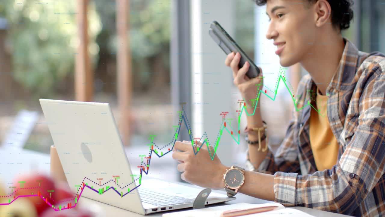 Man tapping phone by window, speaking into phone and generating tech chart over laptop for review