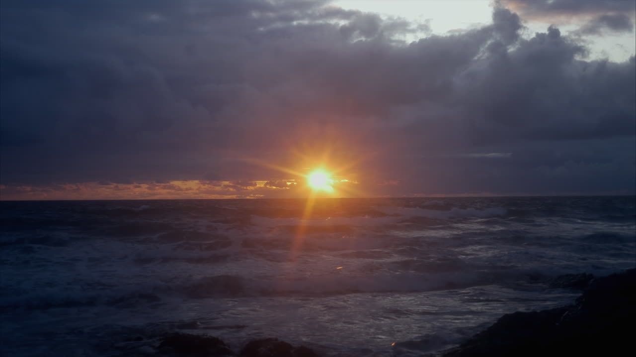 Meereslandschaft mit goldenen Sonnenuntergangsstrahlen, die durch dunkle Wolken scheinen, Statische Aufnahme