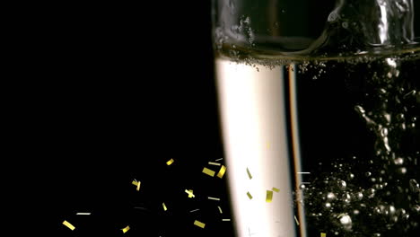 confeti dorado cayendo cerca de las burbujas de champán en un vaso contra un fondo negro