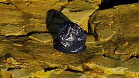 black trash bag lay on a rocky beach