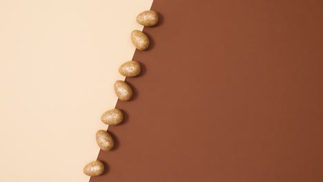 el concepto de colocación plana mínima de huevos de oro de brillo de pascua en movimiento sobre un fondo marrón desnudo.