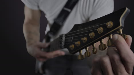 male with tattoos tuning an electric guitar in slow motion with headstock in foreground and in focus