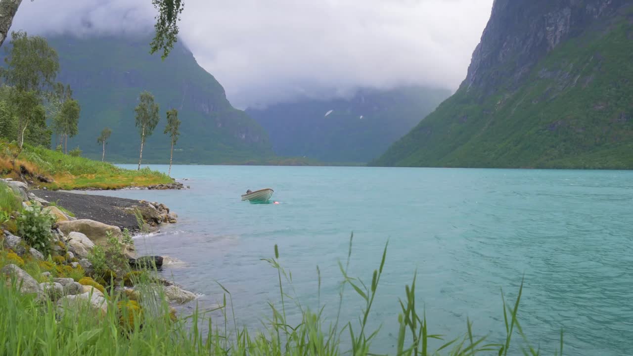 A small boat bobs around in rough water as a storm rolls in over a Norwegian Fjord