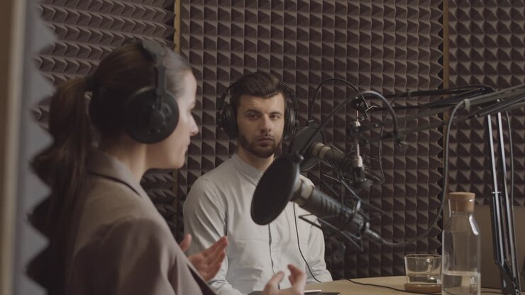 Giovane uomo in uno studio di registrazione radiofonico ascolta le argomentazioni della giovane ed elegante speaker accanto a lui.