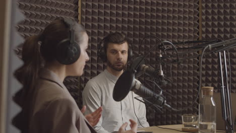 young man in a radio recording studio listens to the arguments of the elegant young female locutor next to him