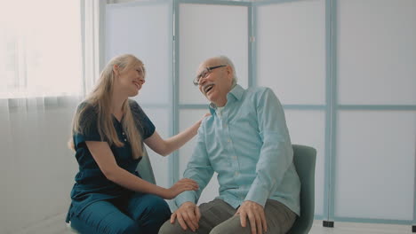 young caring nurse laughing and talking with elderly man in the office