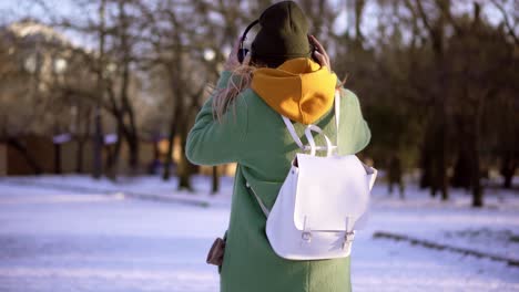 Attractive-girl-walk-in-winter-park,-listening-to-music-on-the-phone,-stylish-look