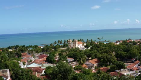 dolly-in ripresa aerea con drone che si avvicina alla bellissima chiesa storica di carmo nel centro della città tropicale costiera di olinda a pernambuco, in brasile, circondata da case residenziali e palme