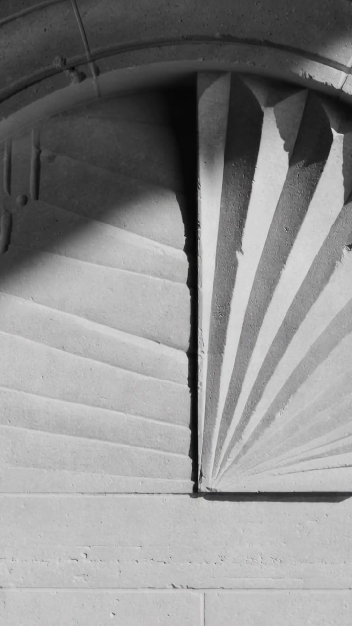 Video verticale: Sole in movimento che proietta un'ombra ad arco su un pannello di pietra sulla facciata, rivelando scanalature a ventaglio.