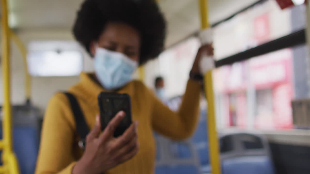 African american businesswoman with face mask using smartphone and standing in bus