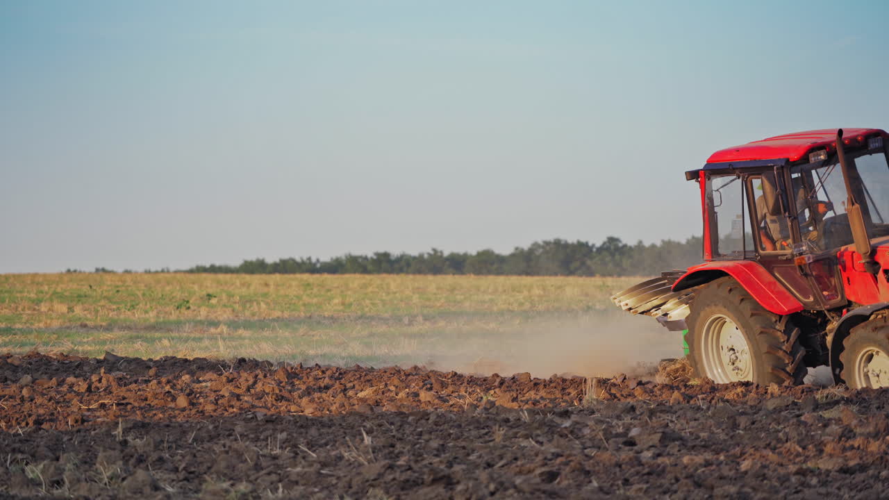 Red tractor in a field. Tractor ploughing a field with a trail of dust behind it