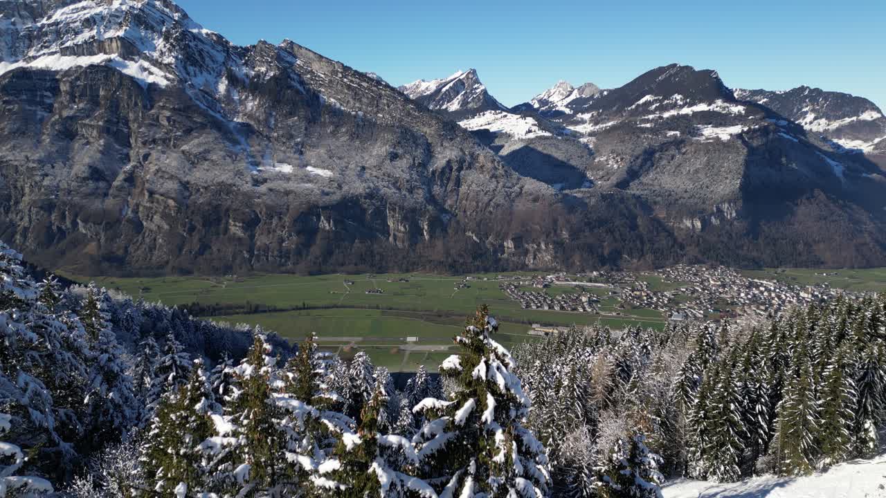 fronalpstock glarus suiza aérea sobre el bosque nevado para revelar la aldea en el valle verde