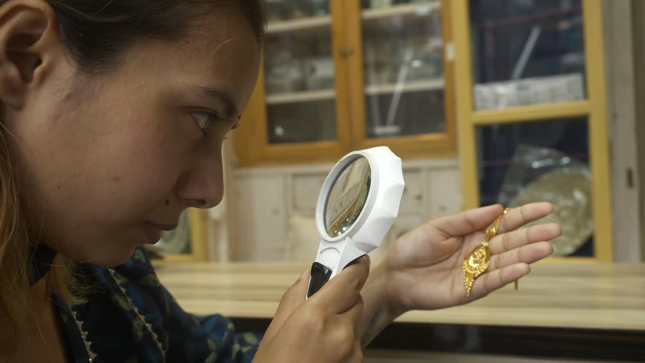 Indian woman checking 18k HUID certified gold jewellery with a magnifying glass at gold shop