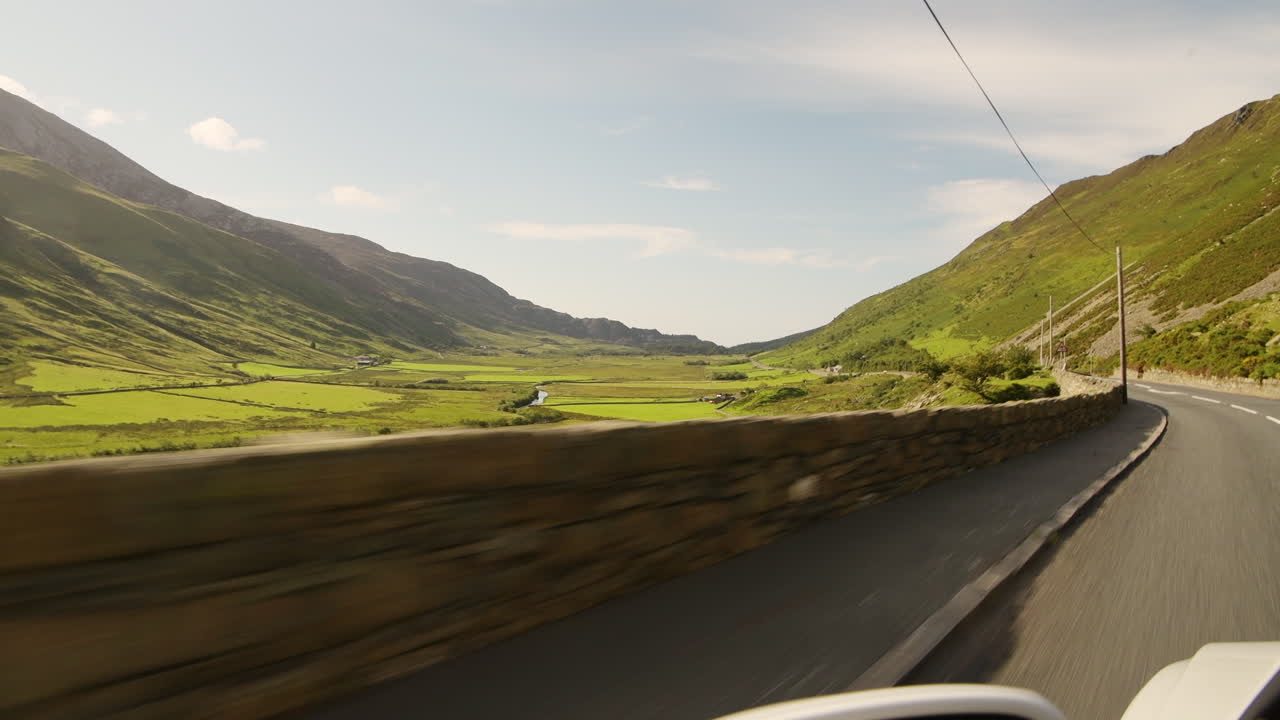Driving through lush countryside valley and mountains in Snowdonia National Park, hanging out of car view speeding along road