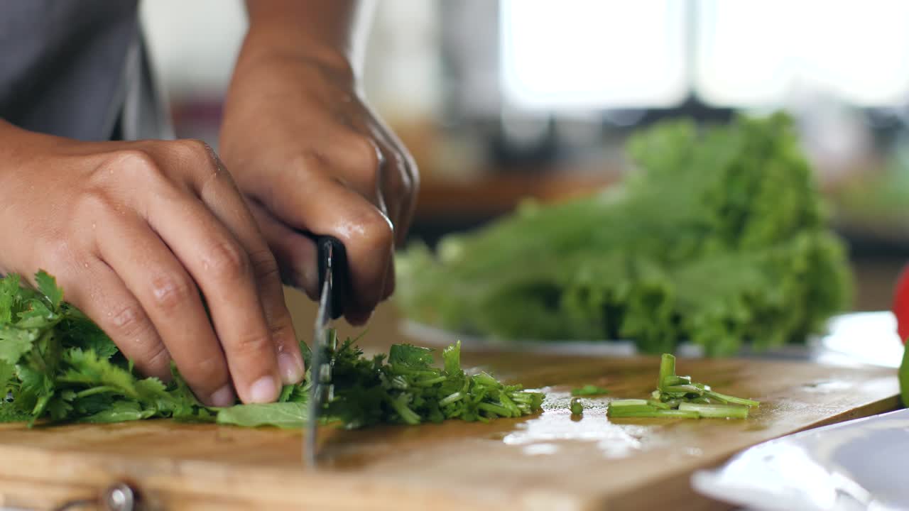 cerca de las manos cortando perejil verde fresco en una tabla de cortar de madera.