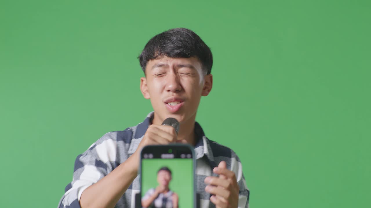 소년 아시아 십대 소년이 마이크를 들고 녹색 화면 배경에서 노래하는 모바일 라이브의 클로즈업