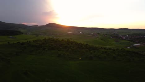 Aerial-shot-of-truck-left-over-open-country-with-fields-and-green-meadows-net-a-town-during-sunset,-Transylvania,-Romania