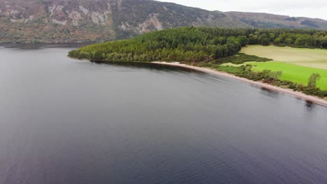 Vista-Aérea-De-La-Playa-Del-Lago-Ness-Con-Paisaje-De-Montaña-En-El-Fondo.