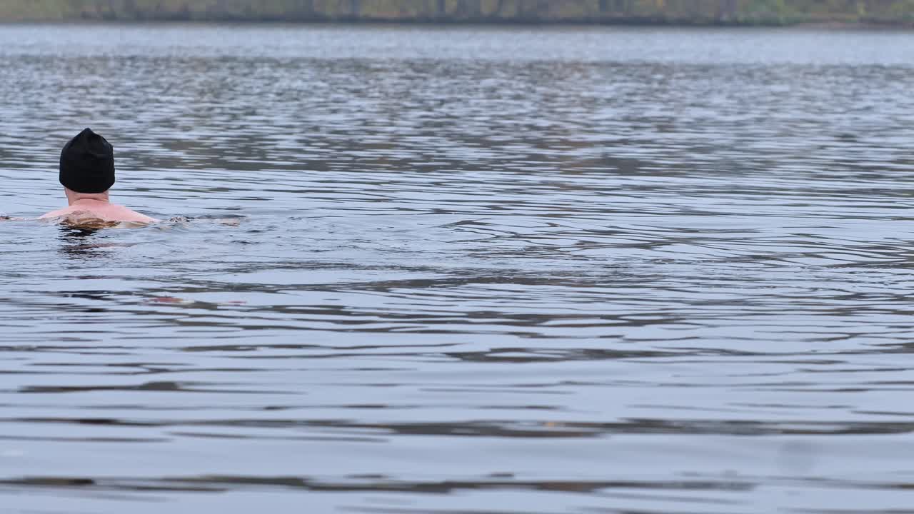 Solitary man swims in cold lake under autumn trees in serene Latvian nature